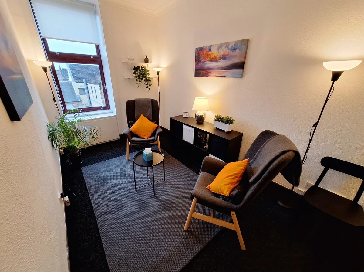 The counselling room at 15 Newton Terrace, Glasgow — two soft armchairs facing each other, warm lamplight, a plant by the tall window and a small table with tissues